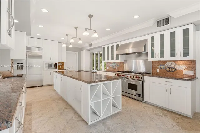 a kitchen with stainless steel appliances granite countertop a stove a sink a refrigerator and white cabinets with wooden floor