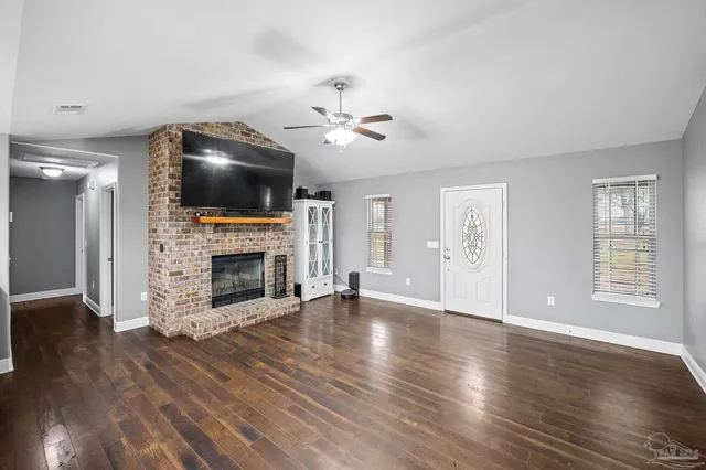 a view of a livingroom with a fireplace a ceiling fan and windows