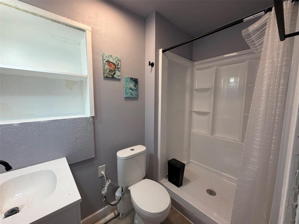 714 Southwest Dallas Street Grand Prairie, TX 75051 - Photo 5 of 27 Bathroom featuring a white vanity with integrated sink, white toilet, and a white shower stall with built-in shelving