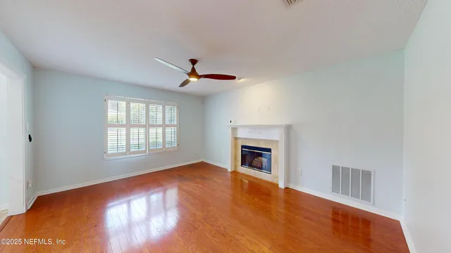 a view of empty room with wooden floor and fan