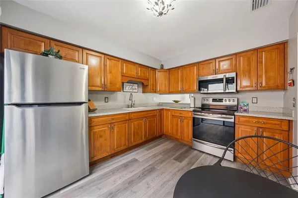 a kitchen with stainless steel appliances granite countertop a refrigerator a stove top oven a sink dishwasher and wooden cabinets with wooden floor