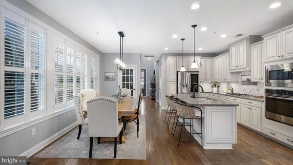 a kitchen with stainless steel appliances granite countertop a stove a sink a refrigerator and a dining table with wooden floor