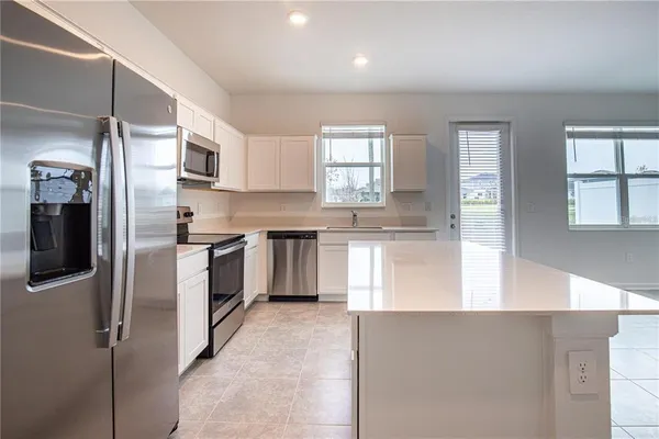 a kitchen with stainless steel appliances kitchen island granite countertop a refrigerator a sink a stove and white cabinets with wooden floor