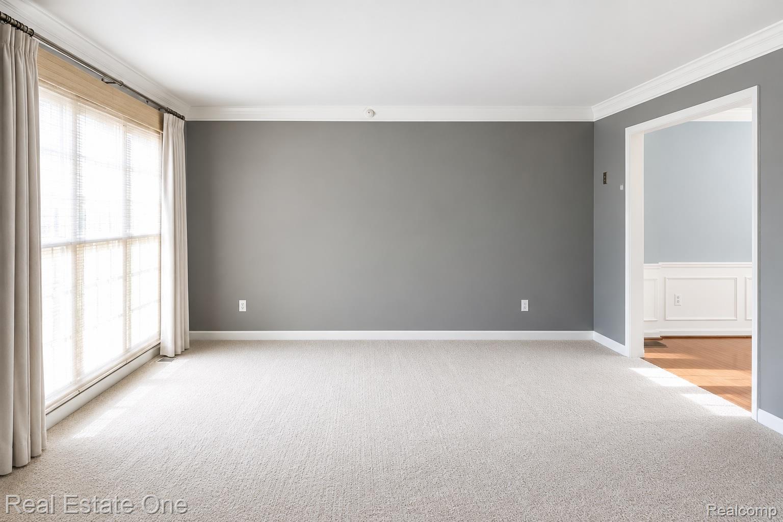 1141 Sandy Ridge Drive Rochester, MI 48306 - Photo 3 of 9 Spacious room with light neutral carpeting, a large window with blinds and drapes, and an entryway featuring wainscoting and wood-finish flooring