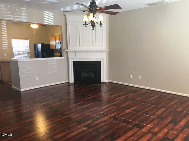 a view of a livingroom with wooden floor a ceiling fan and kitchen view
