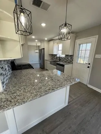 a kitchen with kitchen island granite countertop wooden floor and a refrigerator