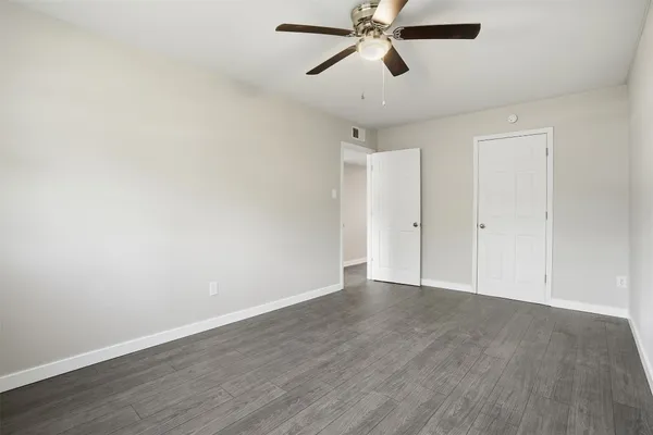 an empty room with wooden floor ceiling fan and windows