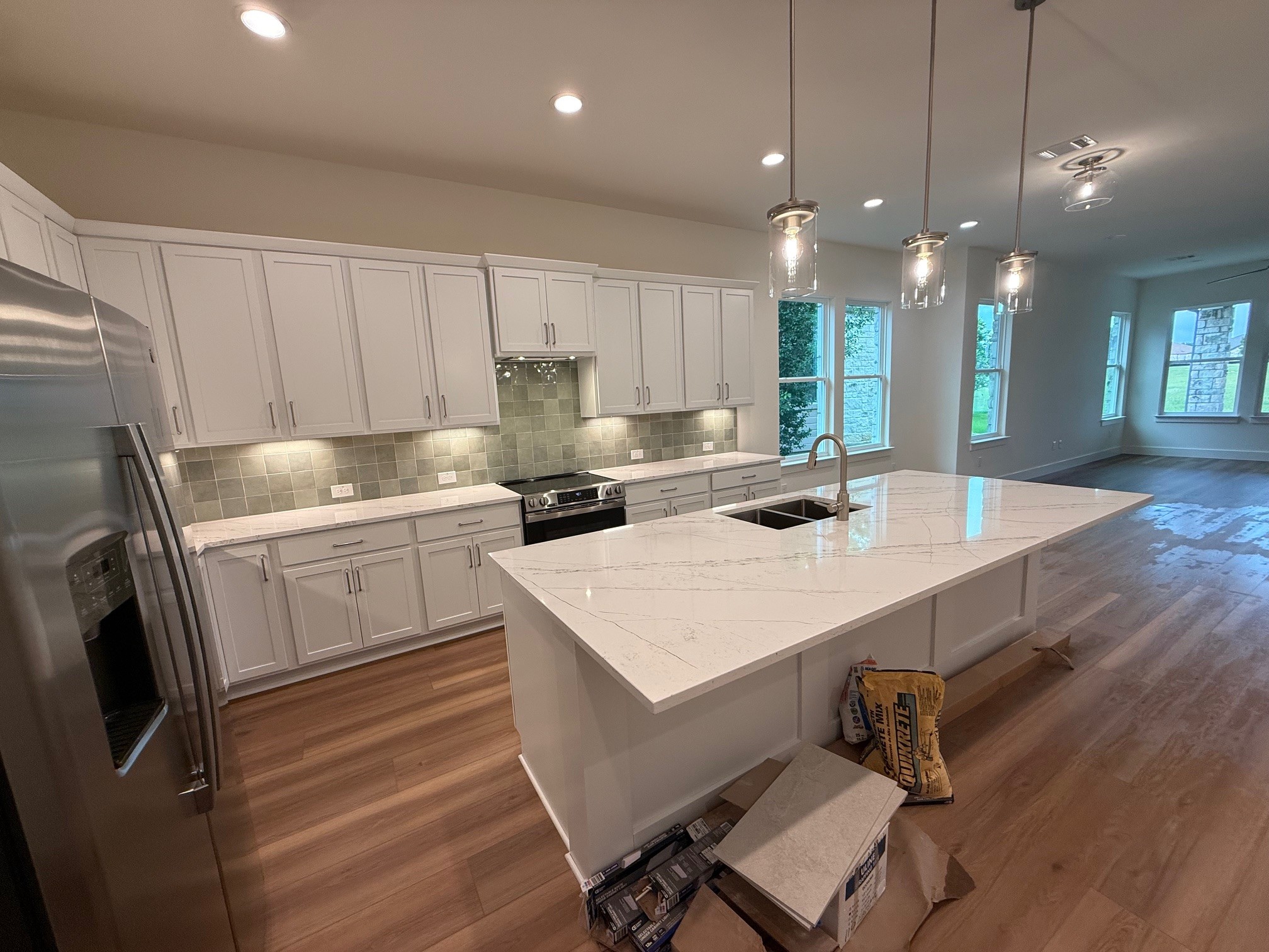 110 Firestone Place Meadowlakes, TX 78654 - Photo 5 of 18 Open-concept kitchen featuring an expansive island with an integrated sink, white shaker cabinetry, stainless steel appliances, wood-finish flooring, and pendant lighting