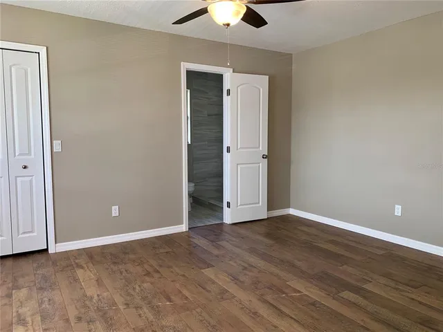 a view of an empty room with wooden floor and a ceiling fan