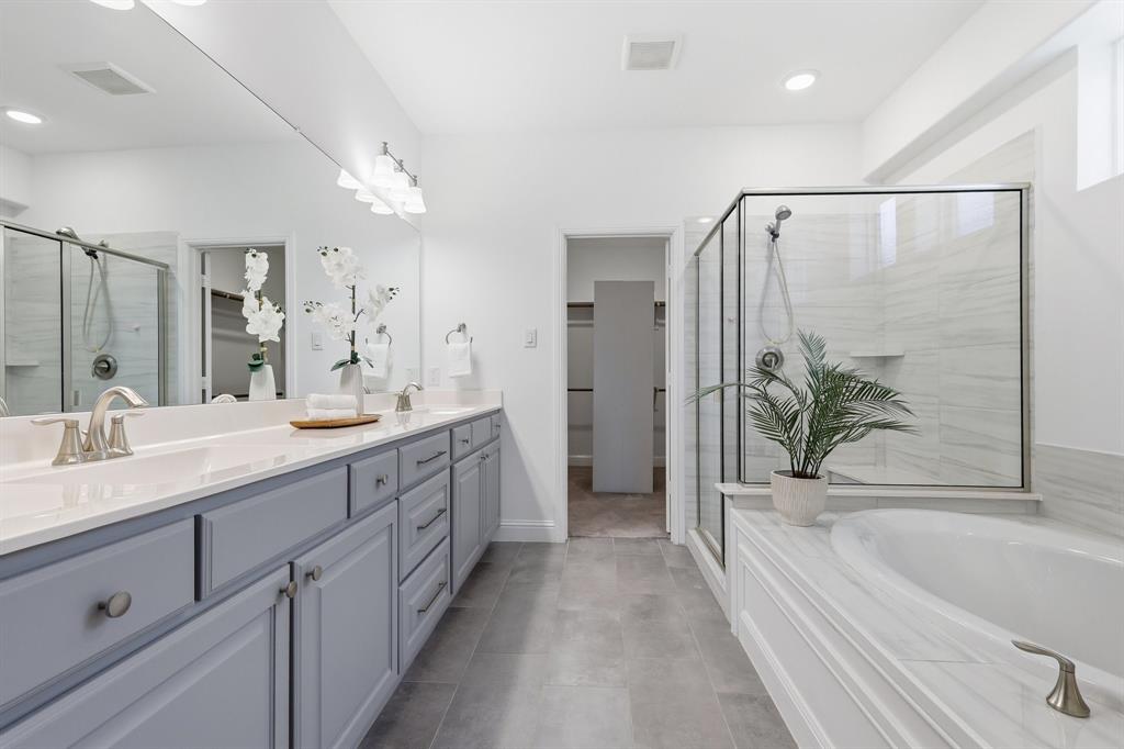 539 Farrell Lane Allen, TX 75013 - Photo 28 of 39 Spacious bathroom featuring a dual vanity with light gray cabinetry and white countertops, a large framed mirror, a separate glass-enclosed shower with subway tile surround, and a built-in soaking tub