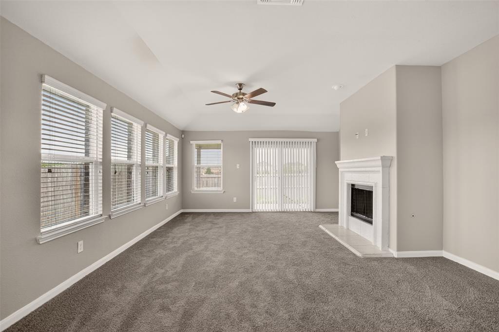 9105 Switchgrass Lane Forney, TX 75126 - Photo 17 of 20 Spacious room featuring gray carpeting, a white mantel fireplace with a dark insert, a ceiling fan with integrated lighting, multiple windows with blinds, and a sliding glass door with vertical blinds