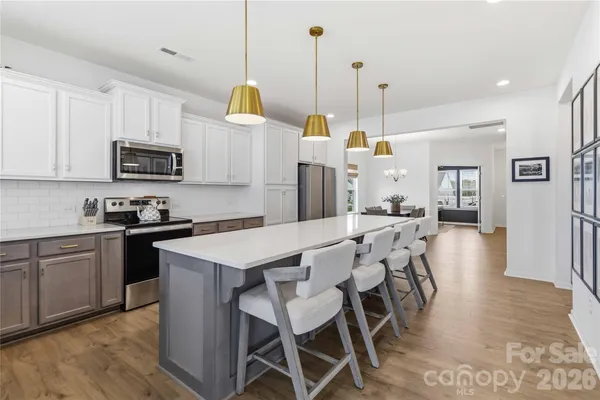 a kitchen with stainless steel appliances granite countertop a stove a sink a microwave a refrigerator a stove and white cabinets with wooden floor