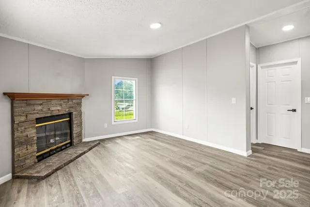 a view of an empty room with wooden floor fireplace and a window