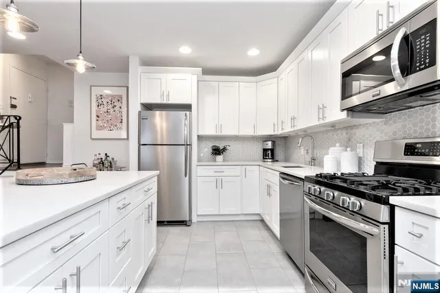 a kitchen with stainless steel appliances granite countertop a sink stove a refrigerator and white cabinets with wooden floor