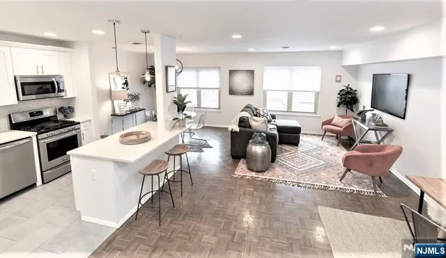 a kitchen with stainless steel appliances kitchen island granite countertop a refrigerator a sink a stove and white cabinets with wooden floor