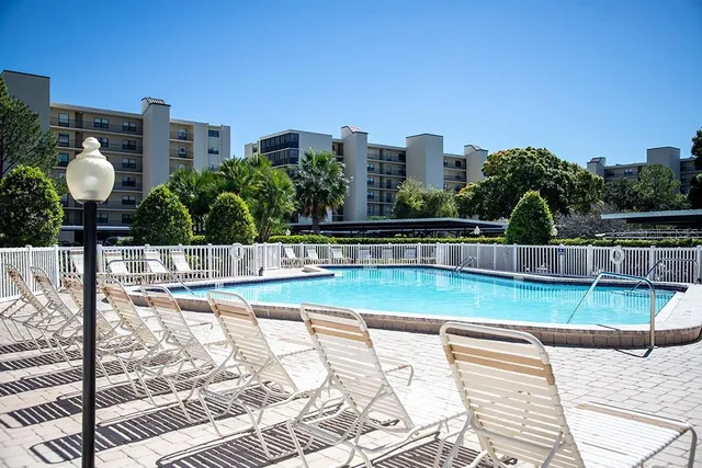 a view of a swimming pool with a bench and trees in the background