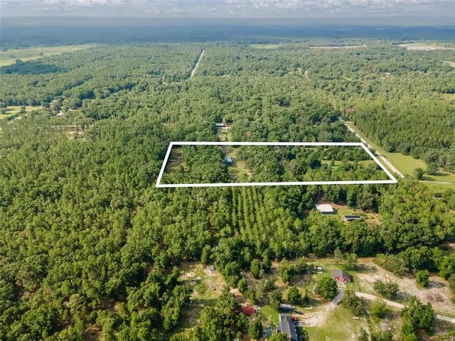 an aerial view of residential house with outdoor space and trees all around