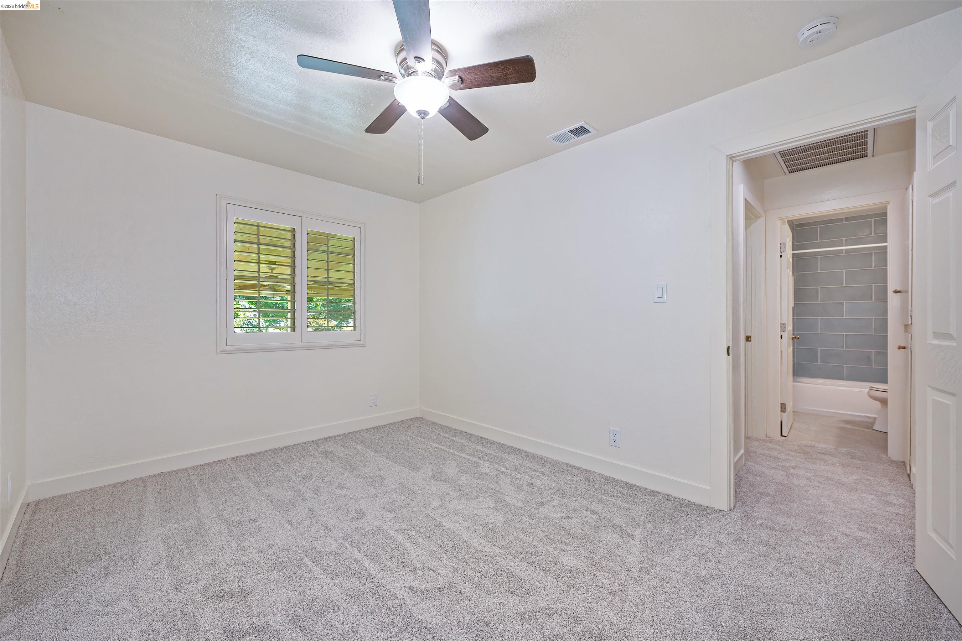 10474 Sheldon Road Elk Grove, CA 95624 - Photo 41 of 83 Carpeted room with a ceiling fan, window with plantation shutters, and a doorway revealing a bathroom with subway tile