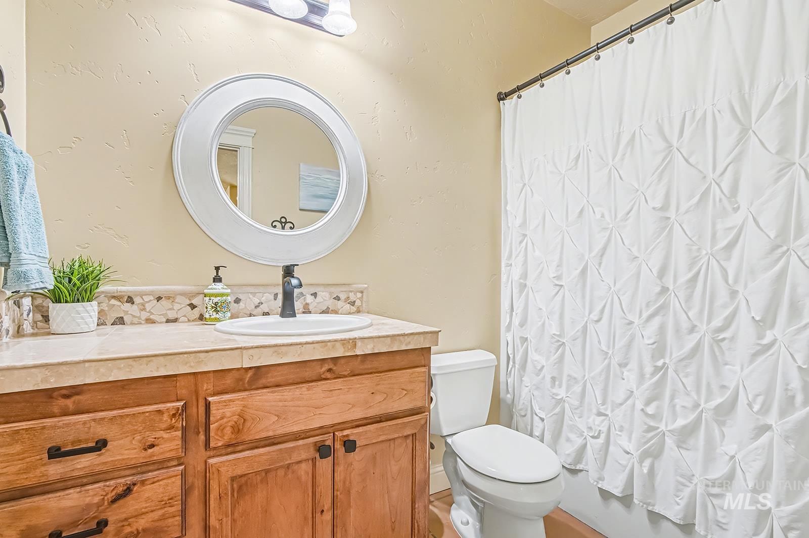 8751 West Rioja Street Star, ID 83669 - Photo 24 of 34 Bathroom vanity featuring a round mirror with a white frame, a single sink with a matte black faucet, and a stone-look countertop with a mosaic tile backsplash