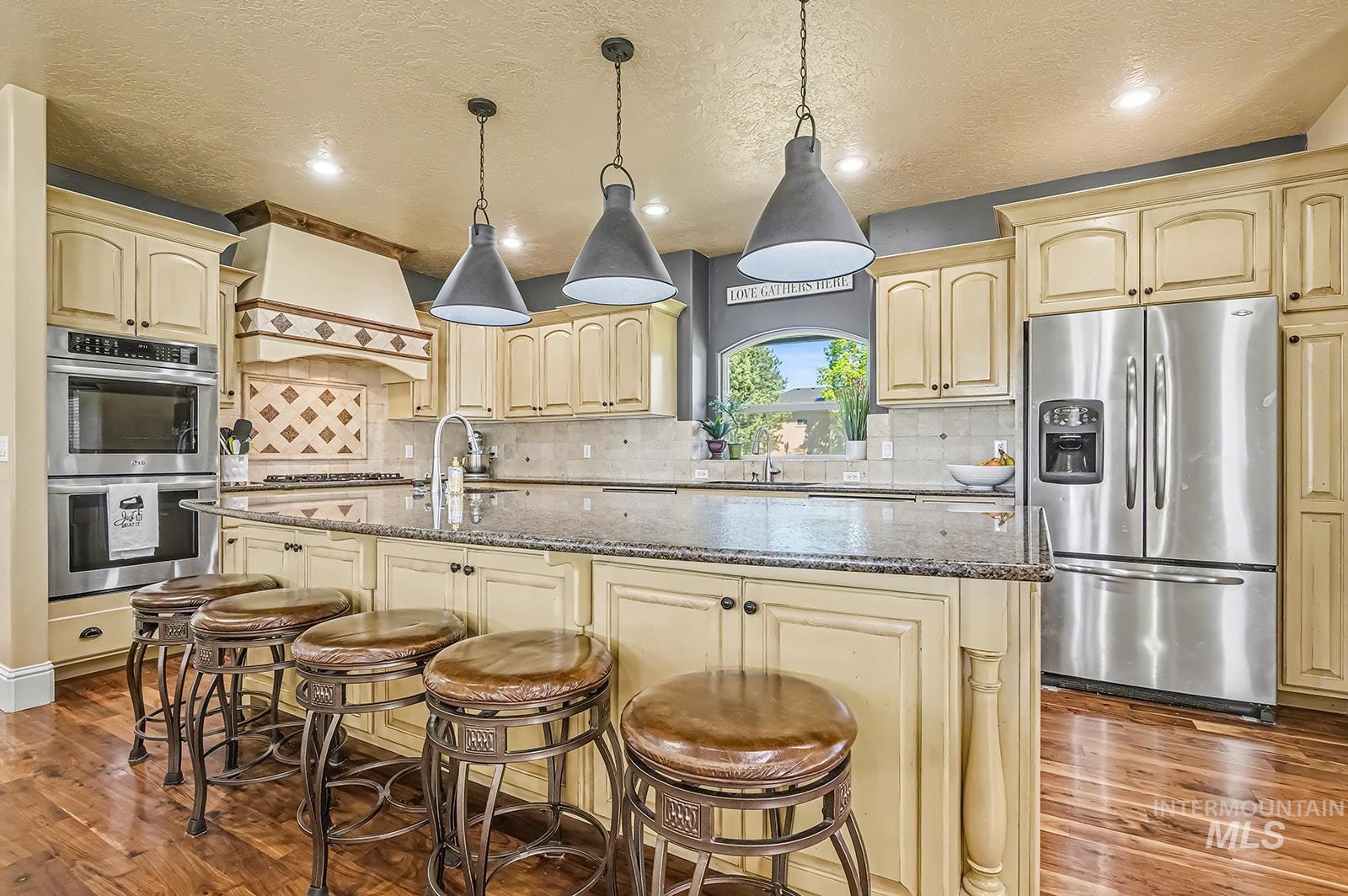 8751 West Rioja Street Star, ID 83669 - Photo 5 of 34 Kitchen featuring an expansive island with a granite countertop, pendant lighting, built-in stainless steel appliances, and wood-finish flooring