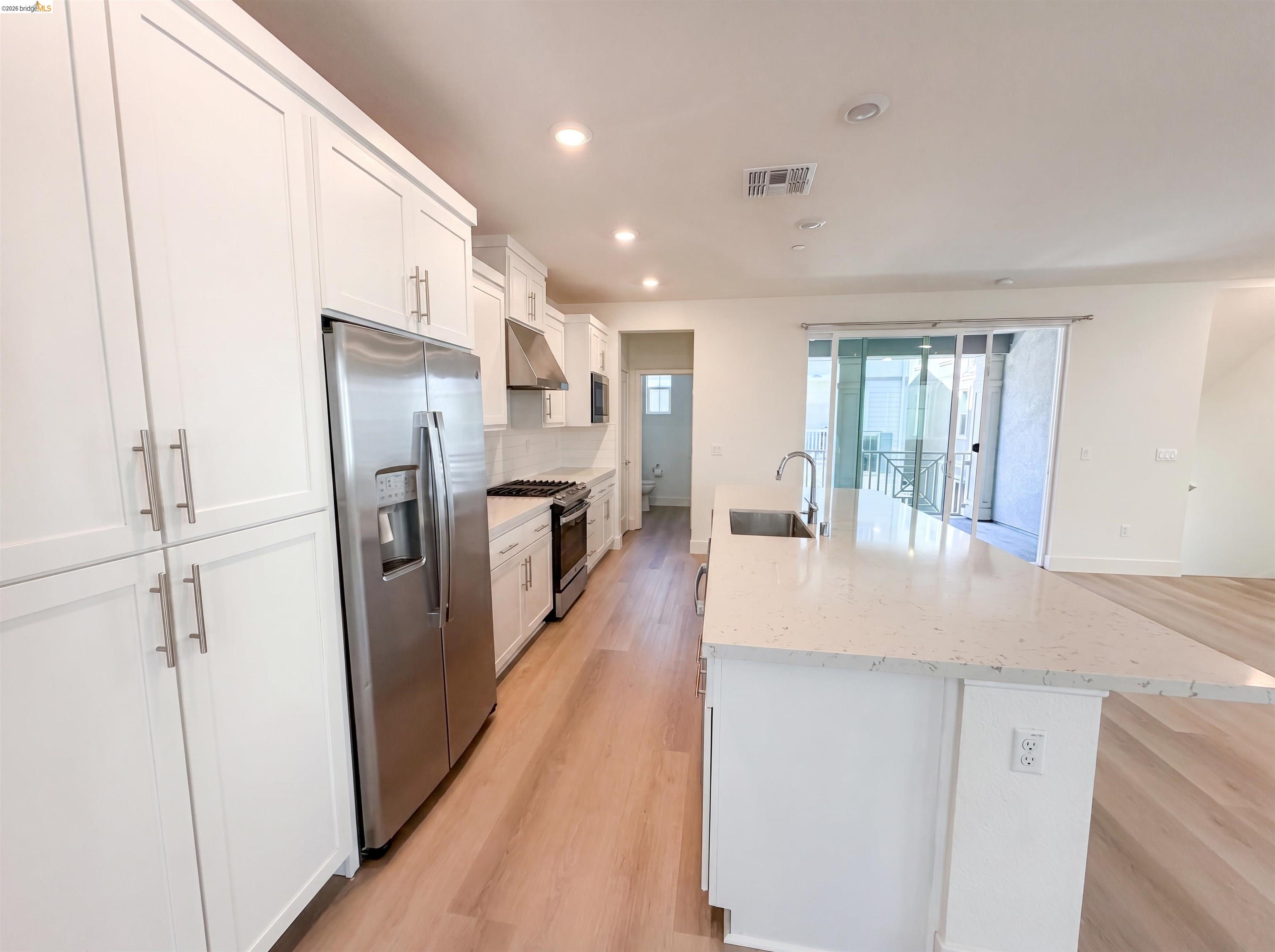 9034 Rudder Way Newark, CA 94560 - Photo 28 of 38 Modern kitchen featuring white shaker cabinetry, stainless steel appliances, a white tile backsplash, and light wood-finish flooring