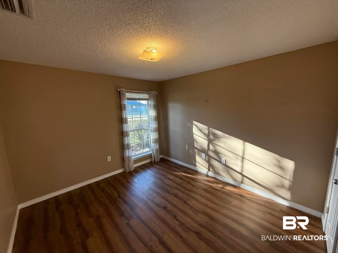 8912 Sherman Road Foley, AL 36535 - Photo 16 of 35 Empty room with dark wood-type flooring, visible vents, a textured ceiling, and baseboards