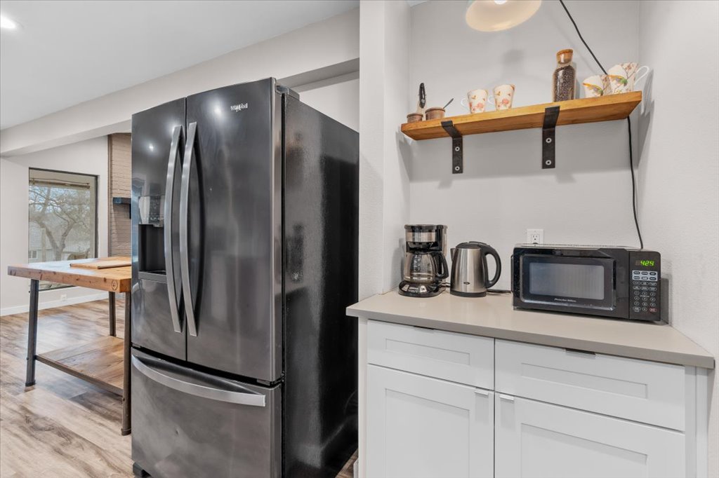 3010 Burleson Road, Unit A Austin, TX 78741 - Photo 13 of 28 Kitchen featuring fridge with ice dispenser, white cabinets, black microwave, open shelves, and light wood-type flooring