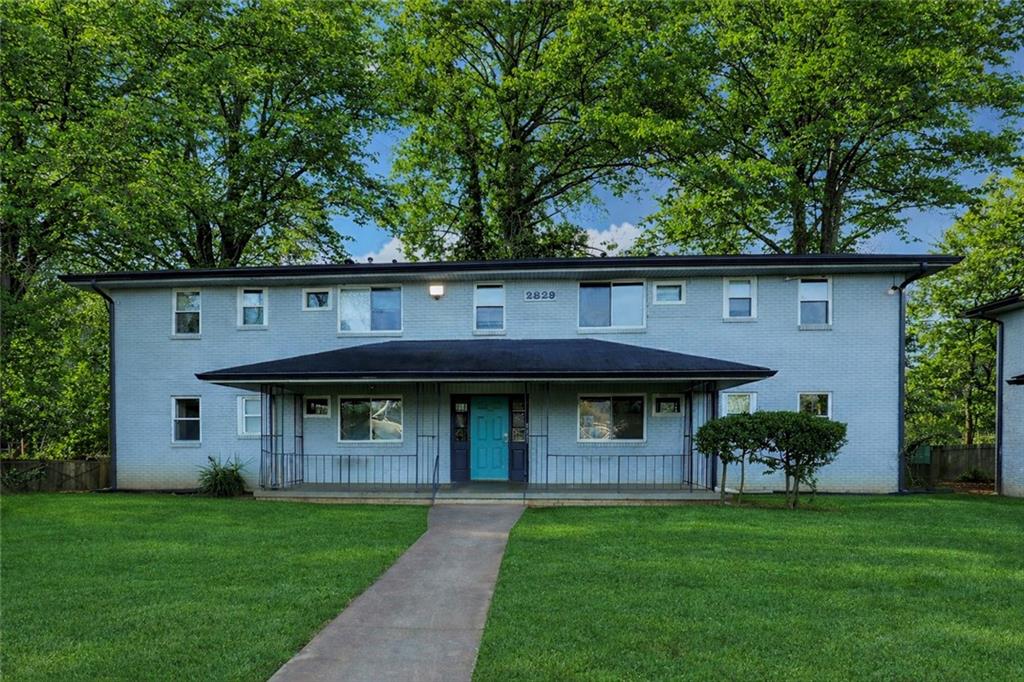 a view of a brick house with a big yard plants and large trees
