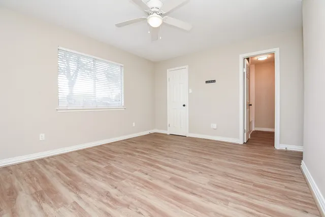 an empty room with wooden floor fan and windows