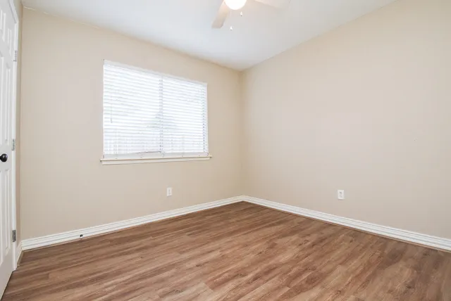 an empty room with wooden floor fan and windows