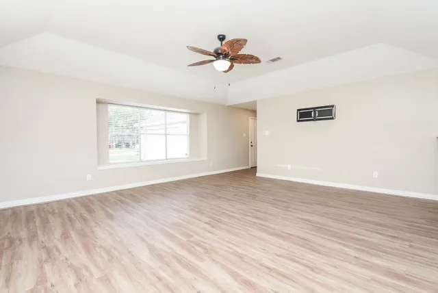 an empty room with wooden floor chandelier fan and windows