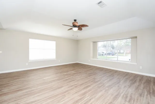 an empty room with wooden floor chandelier fan and windows