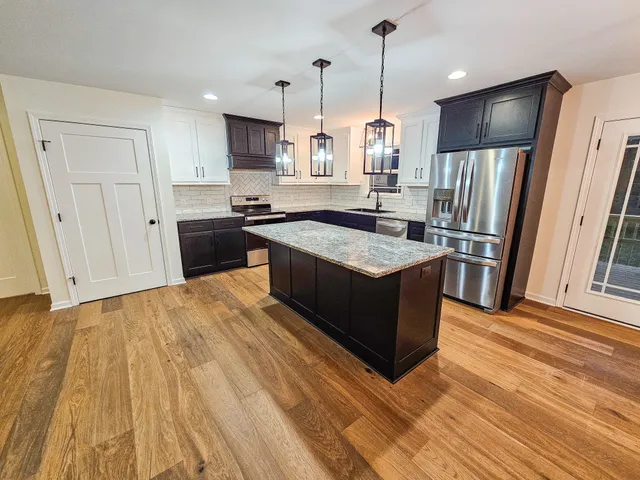 a large kitchen with stainless steel appliances granite countertop a stove a refrigerator a sink and dishwasher with wooden floor