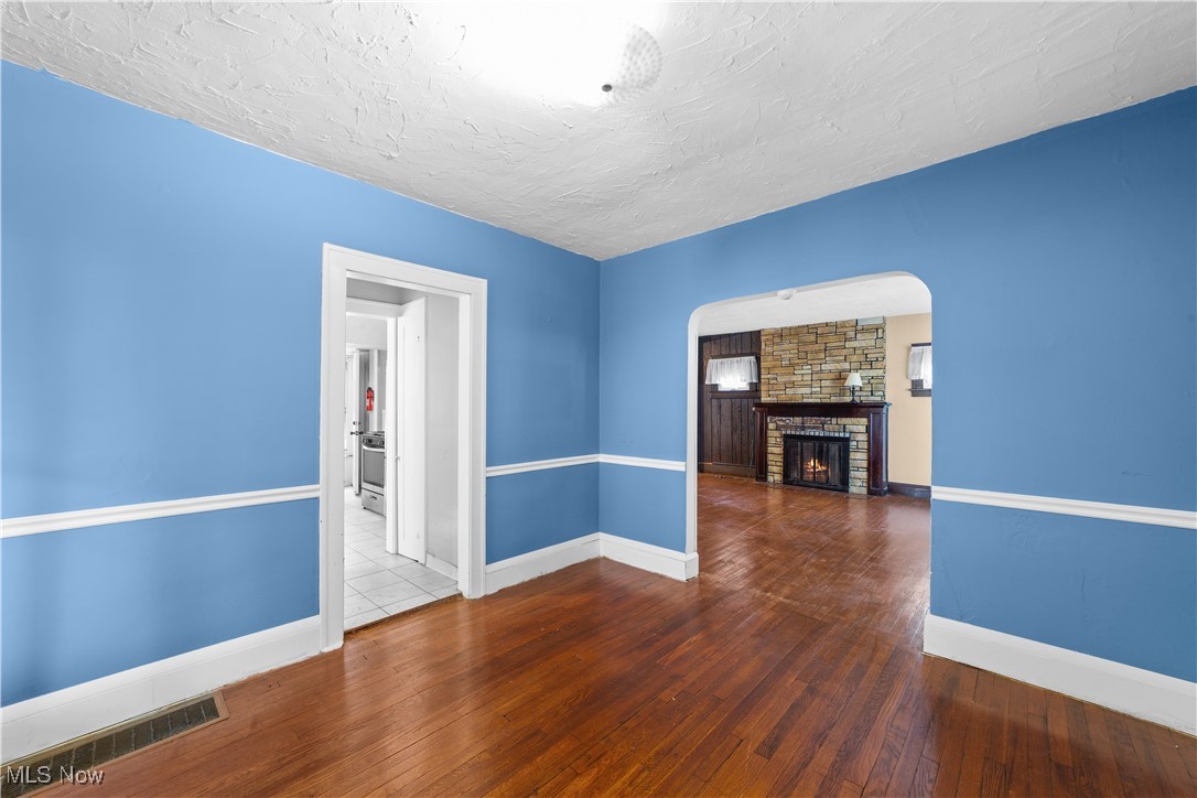 15908 Hazel Road Cleveland, OH 44112 - Photo 8 of 20 Unfurnished living room featuring wood-type flooring, arched walkways, a textured ceiling, and a stone fireplace