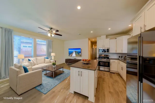 a living room with stainless steel appliances furniture a flat screen tv and a kitchen view