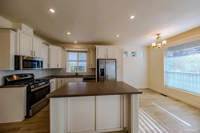 a kitchen with kitchen island granite countertop a stove a sink a refrigerator and white cabinets with wooden floor