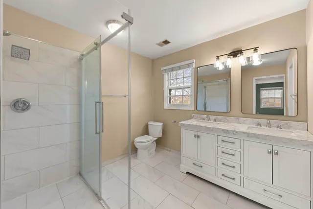 a spacious bathroom with a granite countertop sink a toilet a mirror and a shower