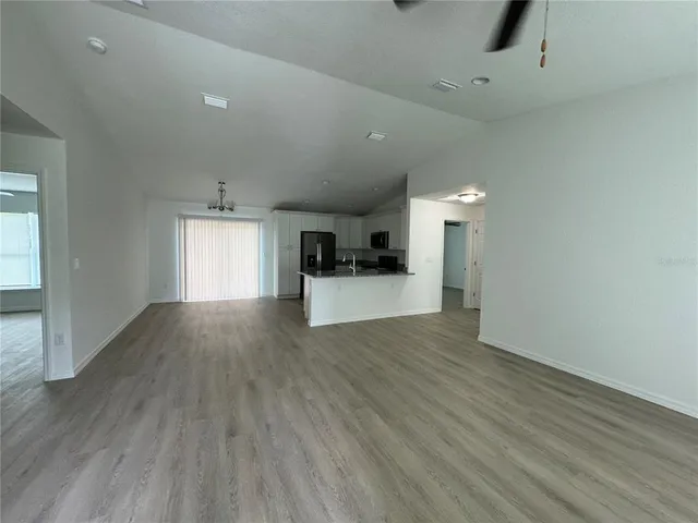 an empty room with wooden floor and kitchen view