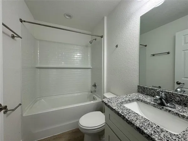 a bathroom with a granite countertop bathtub shower sink vanity mirror and toilet