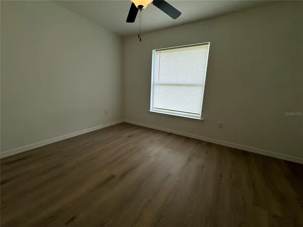 an empty room with wooden floor chandelier fan and windows
