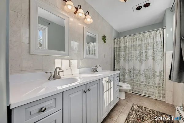 a bathroom with a double vanity sink a toilet a mirror and shower