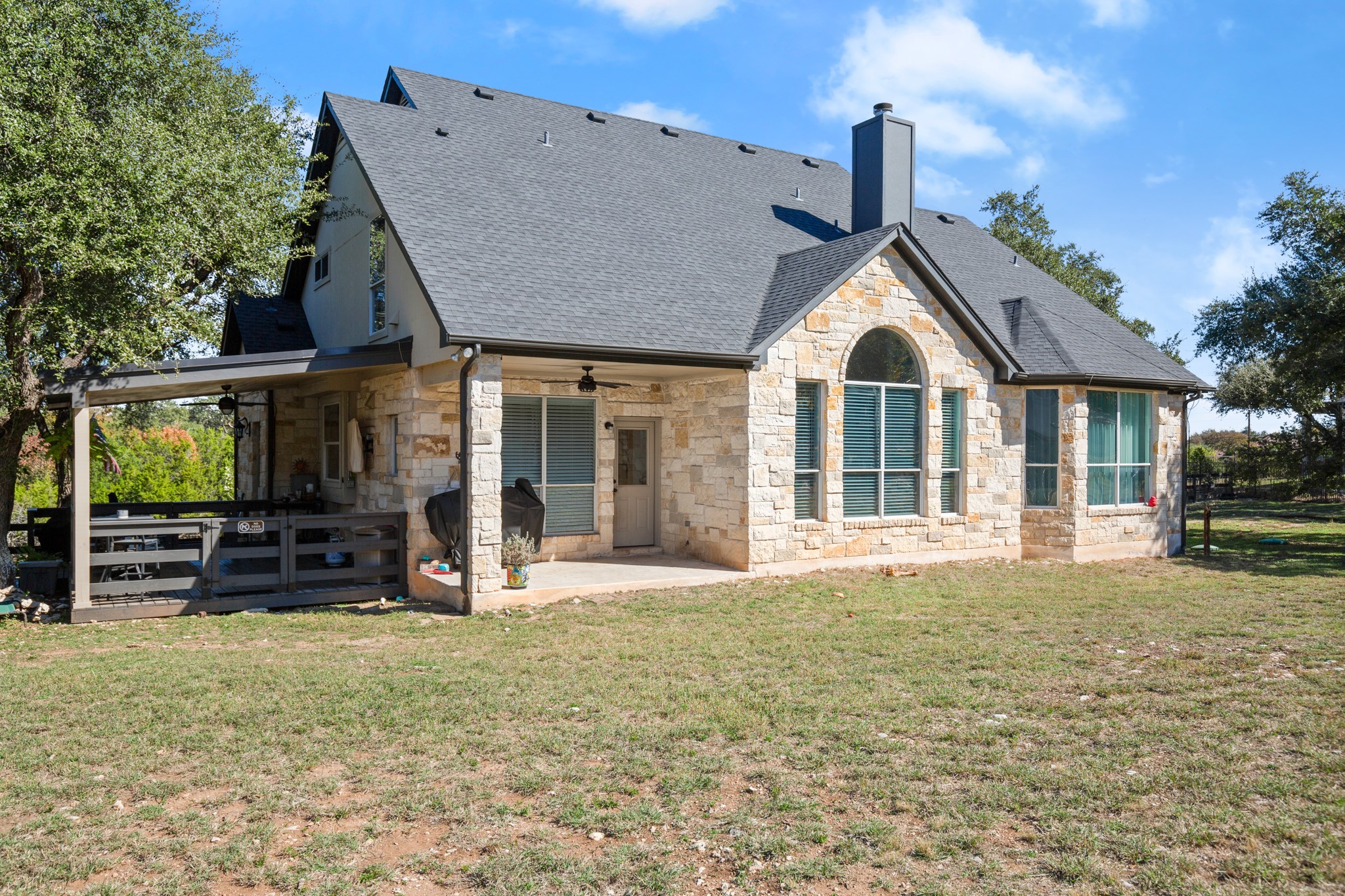 314 Ridge View Drive Georgetown, TX 78628 - Photo 33 of 40 This rear elevation is pure Texas Hill Country architecture, limestone, strong rooflines, a dramatic arched window, and mature trees softening the edges. The covered outdoor living area added in 2025 extends the house toward the yard and gives all that acreage a proper place to be enjoyed.