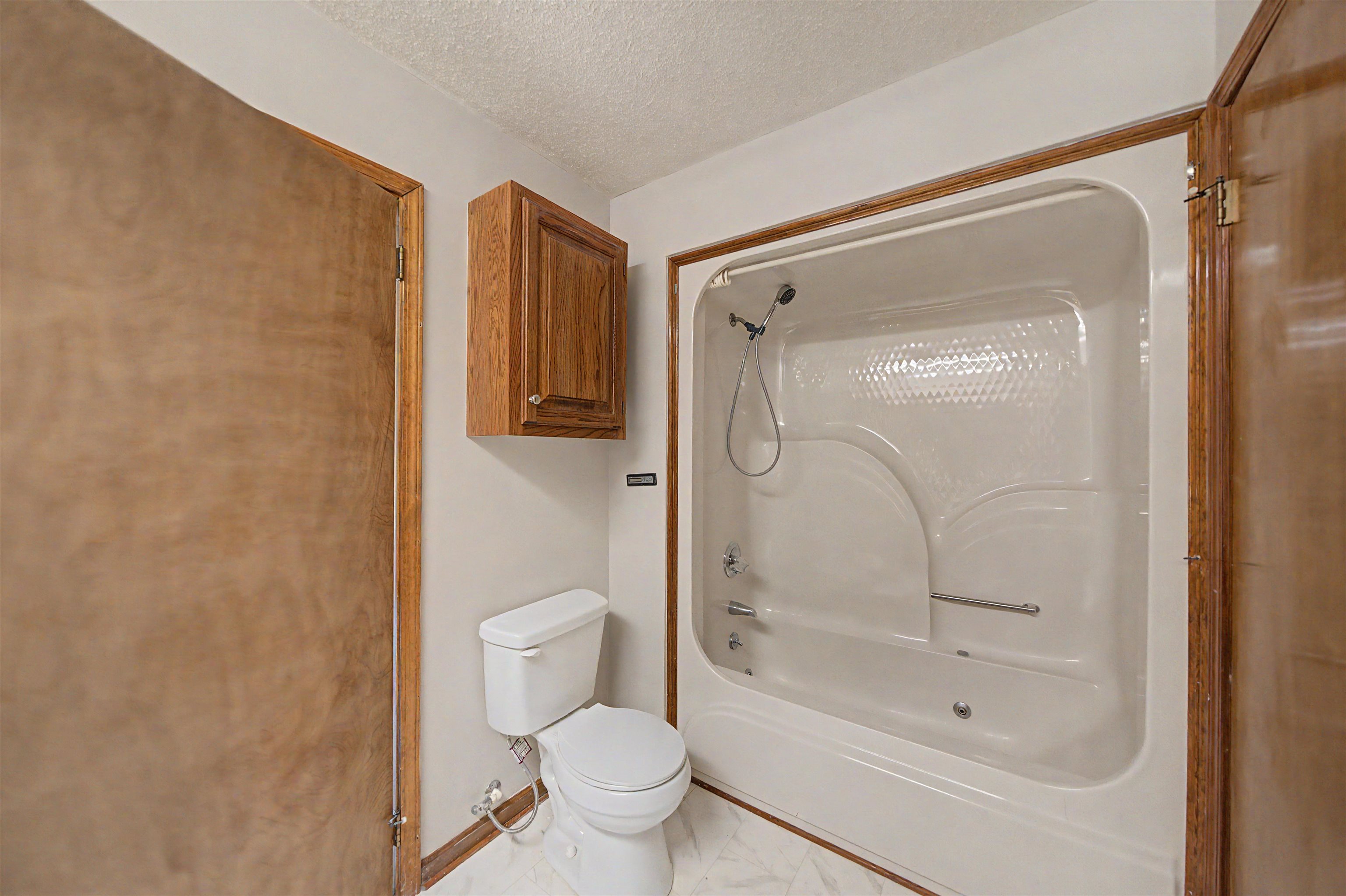162 Lawton Road Selmer, TN 38375 - Photo 21 of 36 Bathroom featuring a white bathtub and shower combination with a textured back panel, chrome fixtures, and a grab bar