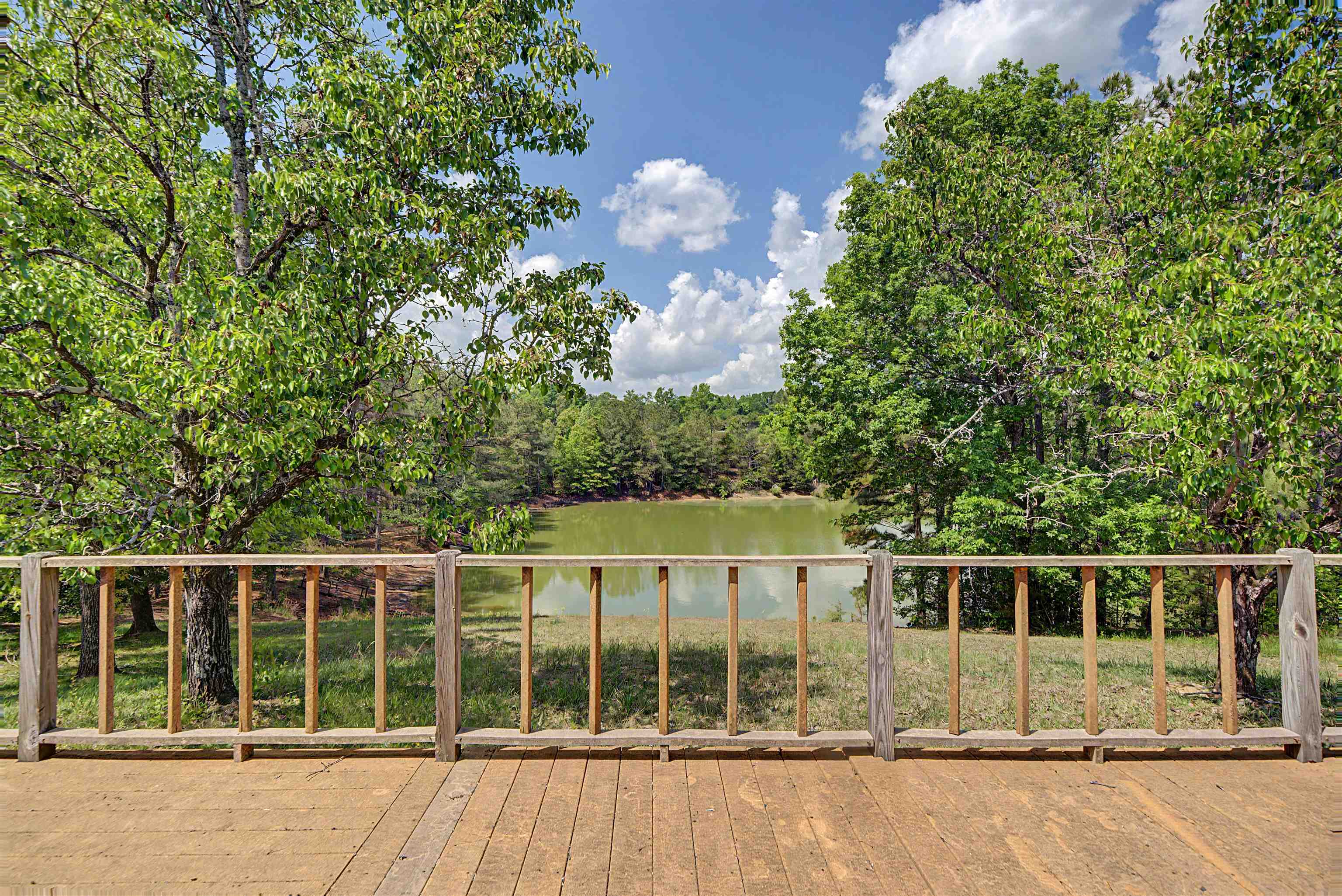 162 Lawton Road Selmer, TN 38375 - Photo 36 of 36 Wood-plank outdoor deck with natural wood railing, surrounded by mature trees, and overlooking a tranquil body of water