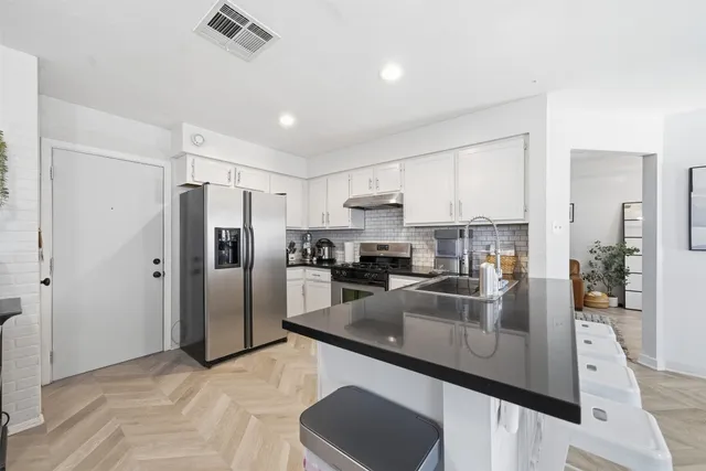 a kitchen with stainless steel appliances granite countertop a refrigerator a sink a stove a oven and white cabinets with wooden floor