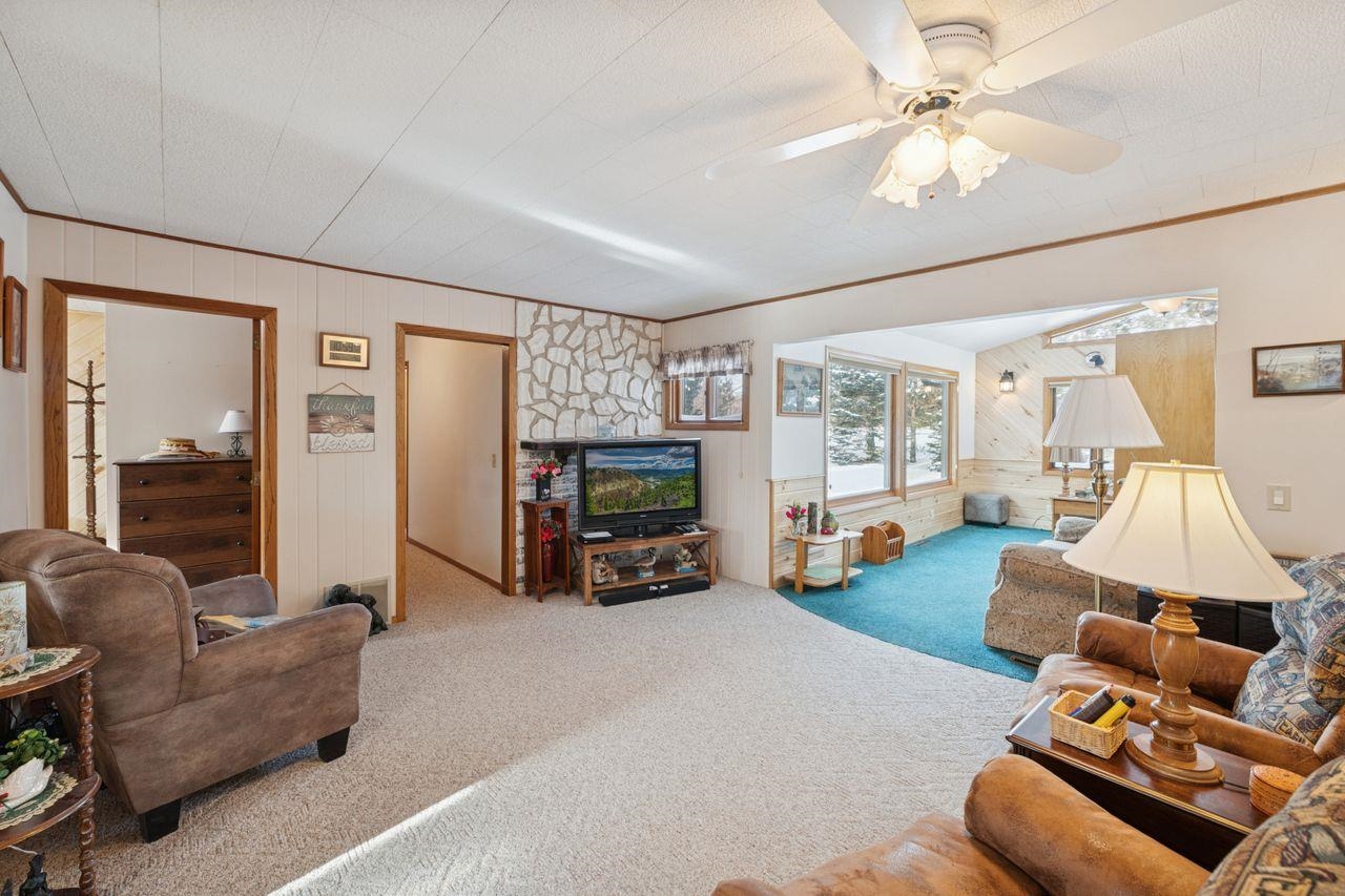 65915 Selke Road Mason, WI 54856 - Photo 11 of 33 Living area featuring wooden walls, carpet floors, ornamental molding, and a ceiling fan