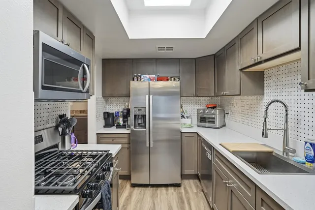 a kitchen with stainless steel appliances a stove a sink dishwasher a refrigerator and cabinets with wooden floor