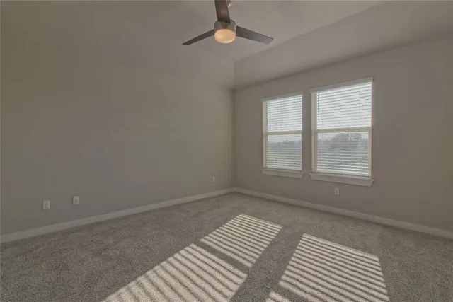 an empty room with wooden floor a ceiling fan and kitchen view