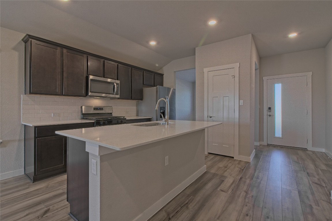 112 Halford Road Georgetown, TX 78633 - Photo 5 of 37 Kitchen featuring dark brown cabinets, stainless steel appliances, tasteful backsplash, a kitchen island with sink, and recessed lighting