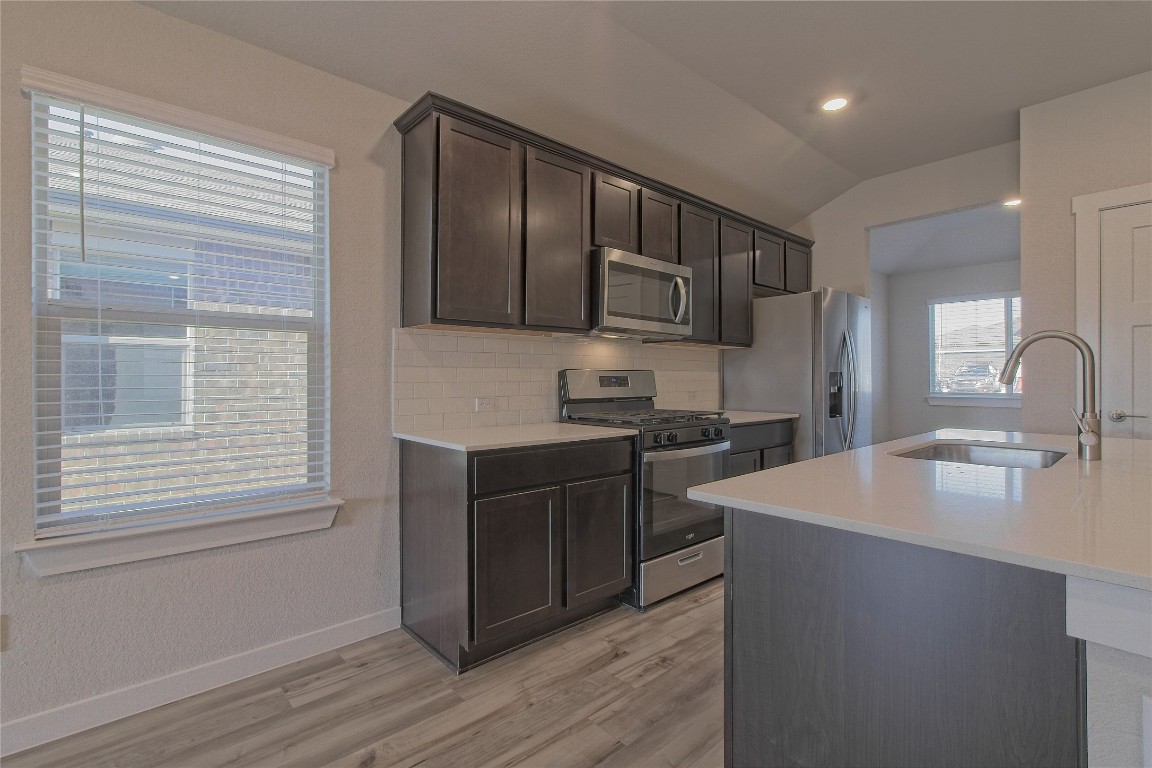 112 Halford Road Georgetown, TX 78633 - Photo 9 of 37 Kitchen with appliances with stainless steel finishes, decorative backsplash, dark brown cabinets, vaulted ceiling, and light stone counters